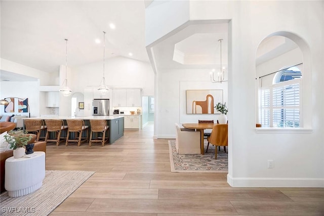 kitchen with light wood-type flooring, a breakfast bar, stainless steel refrigerator with ice dispenser, white cabinets, and light countertops