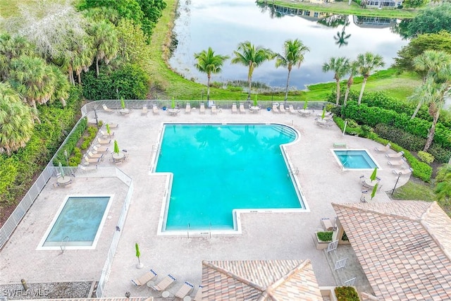 community pool with a patio, fence, and a water view