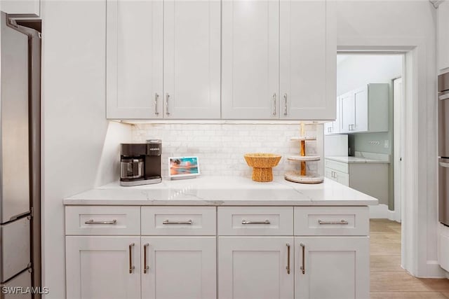 kitchen featuring light stone counters, white cabinetry, backsplash, and freestanding refrigerator