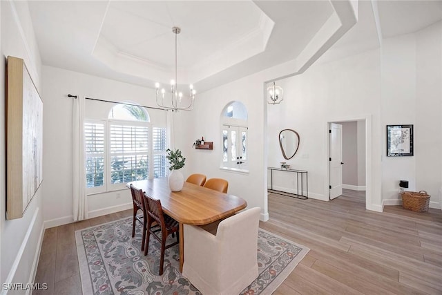 dining room featuring baseboards, a towering ceiling, a raised ceiling, a notable chandelier, and light wood-type flooring