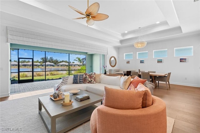 living area with a raised ceiling, a ceiling fan, wood finished floors, recessed lighting, and baseboards