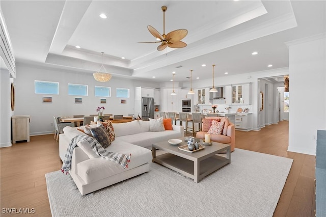 living room with light wood-type flooring, ornamental molding, a tray ceiling, recessed lighting, and ceiling fan