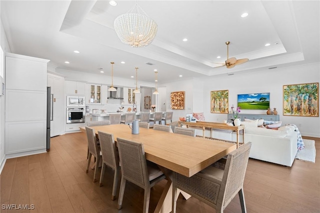 dining area with recessed lighting, ceiling fan with notable chandelier, light wood-type flooring, and a raised ceiling