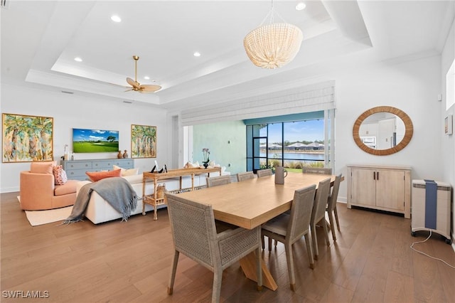 dining space with light wood finished floors, recessed lighting, ceiling fan with notable chandelier, and a tray ceiling