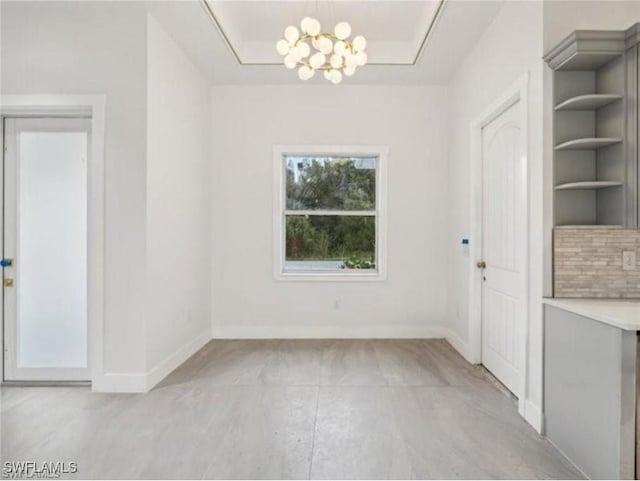 unfurnished dining area featuring an inviting chandelier, a tray ceiling, and baseboards