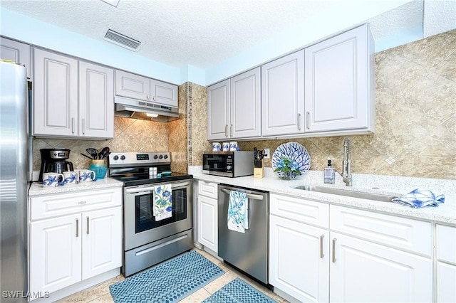 kitchen featuring visible vents, under cabinet range hood, decorative backsplash, appliances with stainless steel finishes, and a sink