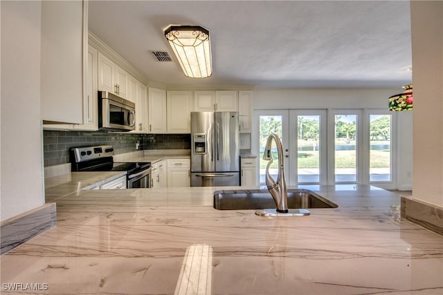 kitchen with visible vents, decorative backsplash, appliances with stainless steel finishes, white cabinets, and a sink