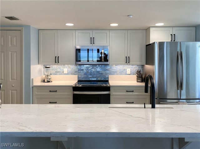 kitchen featuring stainless steel appliances, light stone countertops, tasteful backsplash, and visible vents