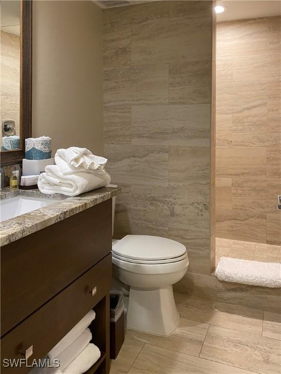 full bathroom featuring toilet, tile walls, vanity, and a tile shower