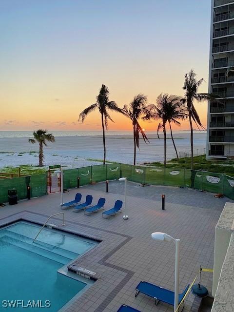 pool at dusk featuring a patio area, fence, a community pool, and a water view