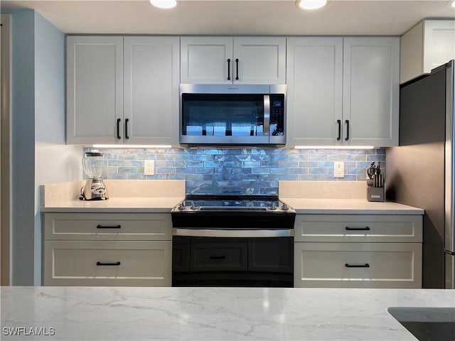 kitchen with decorative backsplash, light stone countertops, appliances with stainless steel finishes, and white cabinets