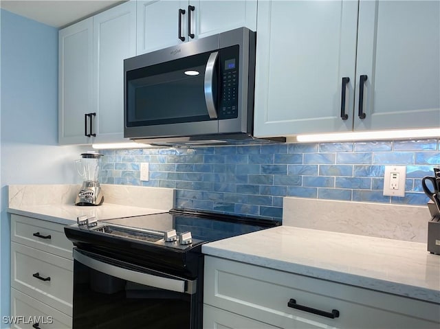 kitchen featuring tasteful backsplash, stainless steel microwave, light stone countertops, black electric range oven, and white cabinetry