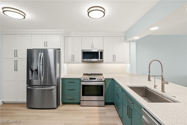 kitchen with green cabinets, light wood-type flooring, white cabinets, stainless steel appliances, and a sink