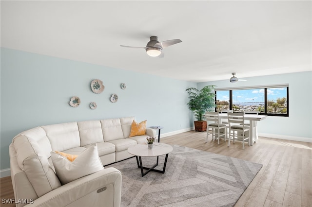 living room featuring baseboards, light wood-type flooring, and ceiling fan