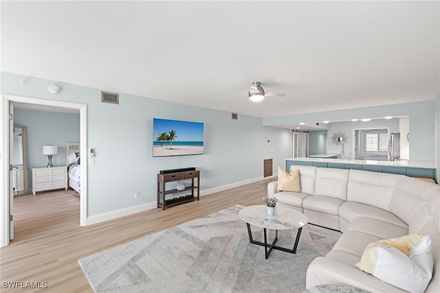 living room featuring visible vents, light wood-style flooring, baseboards, and a ceiling fan