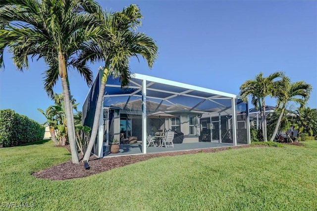 rear view of house featuring a patio, a lawn, and a lanai