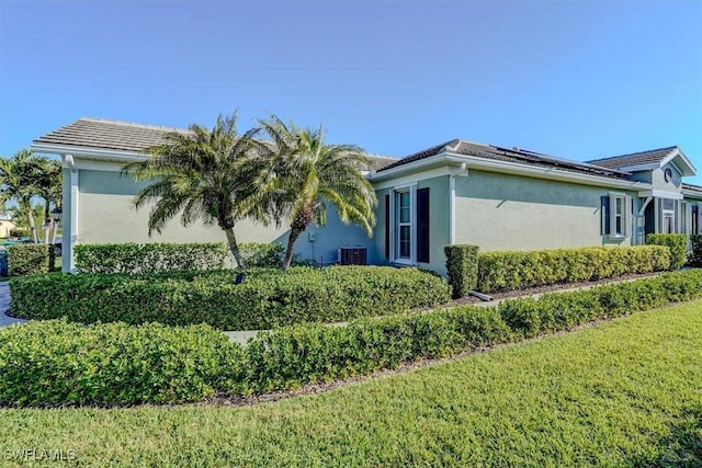 view of side of property featuring stucco siding, a lawn, a tile roof, roof mounted solar panels, and central AC