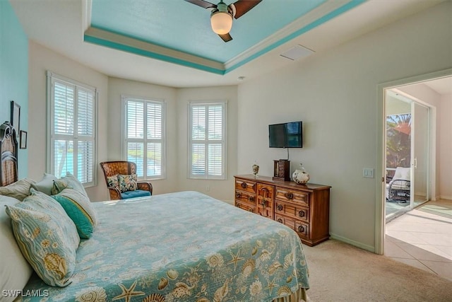 bedroom featuring baseboards, light carpet, light tile patterned floors, a raised ceiling, and a ceiling fan