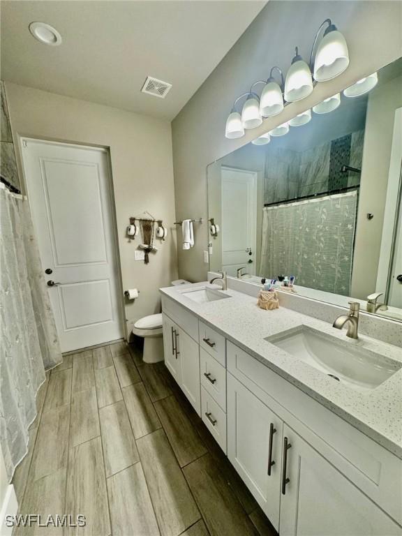 bathroom featuring a tile shower, visible vents, toilet, and a sink