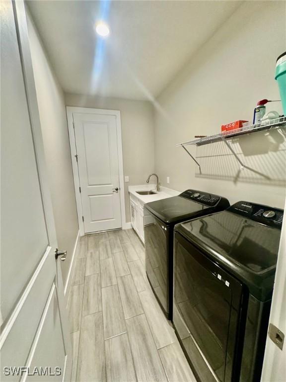 laundry area with baseboards, wood finish floors, cabinet space, independent washer and dryer, and a sink