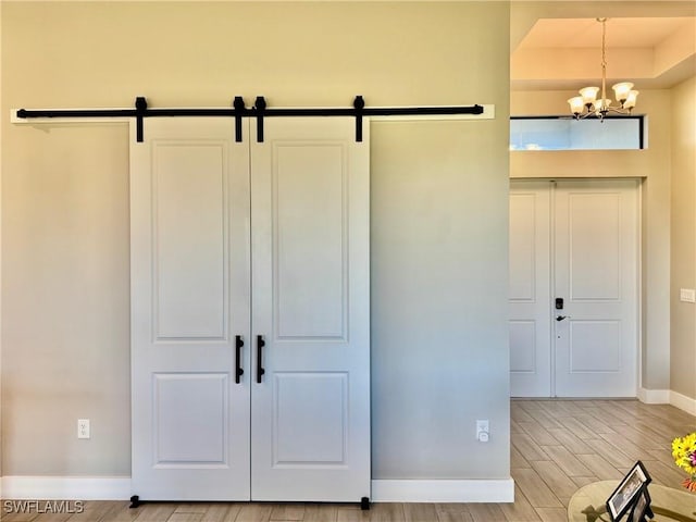 interior space featuring a barn door, a notable chandelier, baseboards, and light wood-type flooring