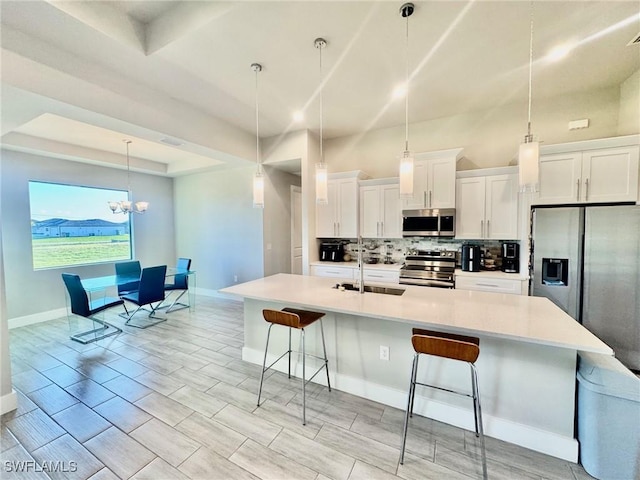 kitchen featuring a kitchen bar, a sink, tasteful backsplash, white cabinetry, and appliances with stainless steel finishes