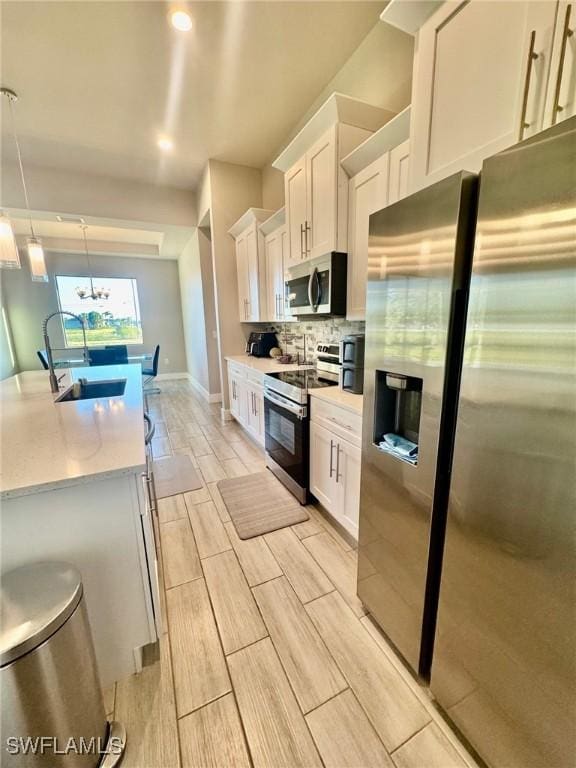 kitchen featuring light countertops, decorative backsplash, appliances with stainless steel finishes, white cabinetry, and a sink