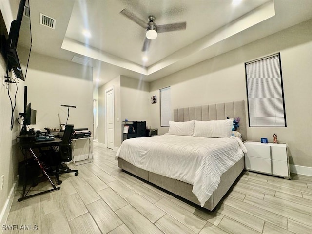 bedroom with visible vents, ceiling fan, baseboards, wood tiled floor, and a raised ceiling