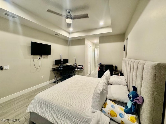 bedroom with light wood-type flooring, visible vents, a raised ceiling, baseboards, and ceiling fan