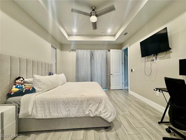 bedroom featuring wood finish floors, visible vents, a tray ceiling, baseboards, and ceiling fan