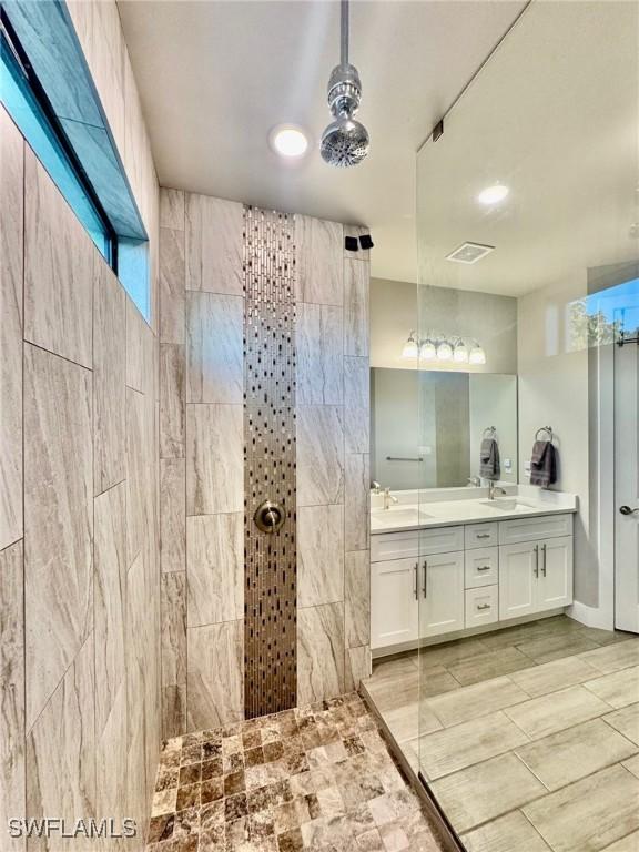 full bath with a tile shower, a sink, visible vents, and double vanity