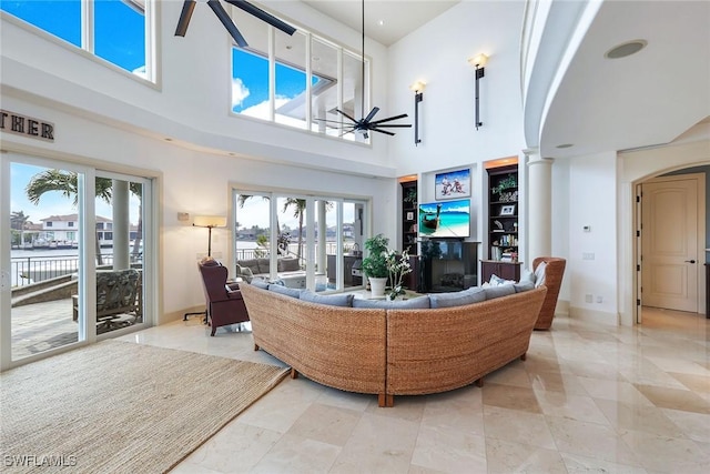 living area featuring baseboards, a fireplace, a high ceiling, a ceiling fan, and ornate columns