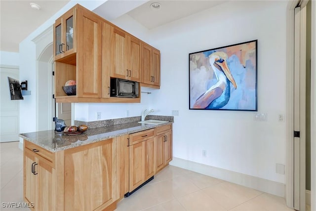 kitchen with a sink, black microwave, light tile patterned floors, glass insert cabinets, and light stone countertops