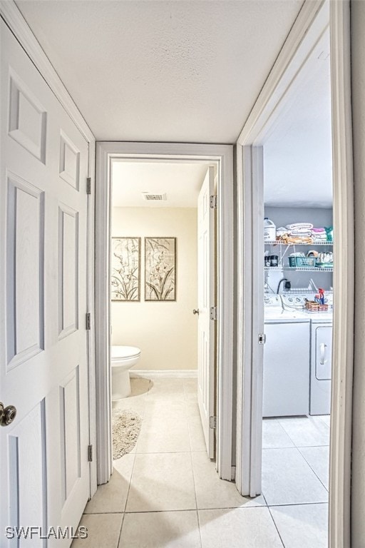 hallway featuring visible vents, baseboards, light tile patterned floors, independent washer and dryer, and a textured ceiling