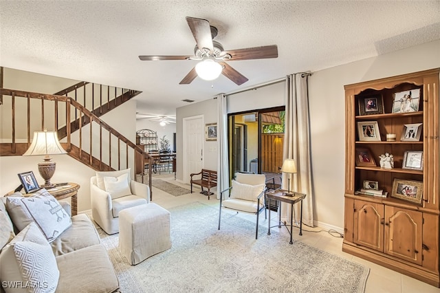 living area with a ceiling fan, baseboards, light tile patterned flooring, stairs, and a textured ceiling