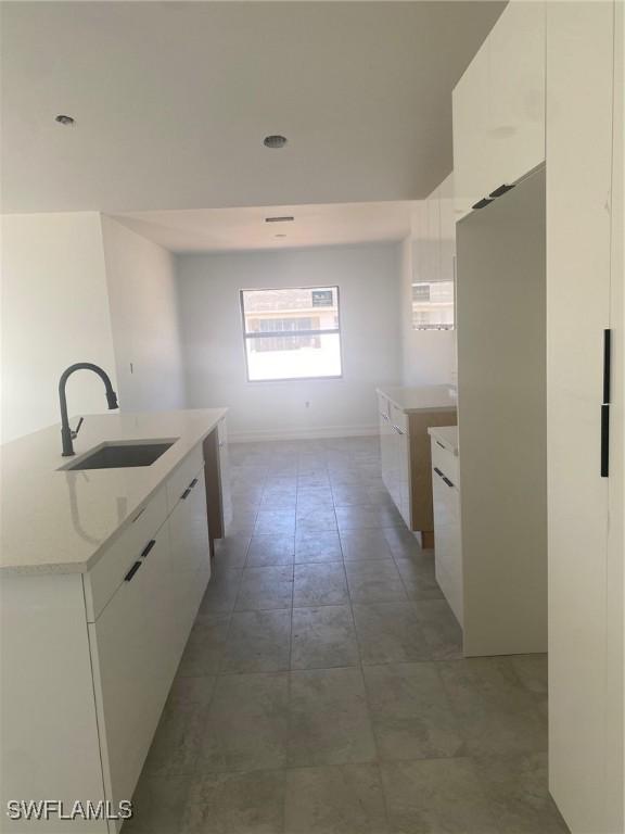 kitchen with light stone countertops, an island with sink, white cabinets, modern cabinets, and a sink