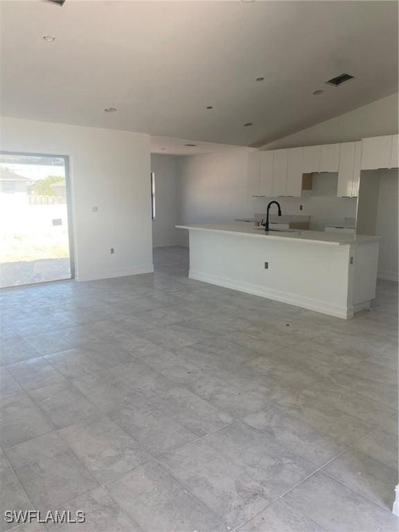 unfurnished living room featuring a sink, visible vents, lofted ceiling, and baseboards