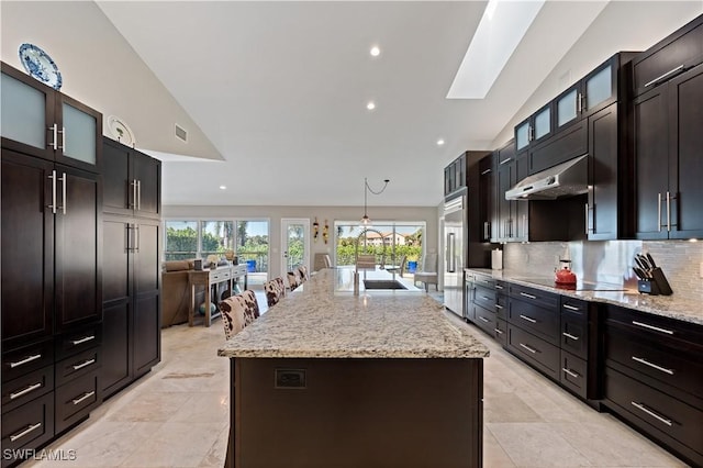 kitchen featuring stainless steel built in fridge, under cabinet range hood, a sink, tasteful backsplash, and black electric cooktop