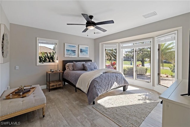 bedroom with access to exterior, multiple windows, light wood-style floors, and ceiling fan