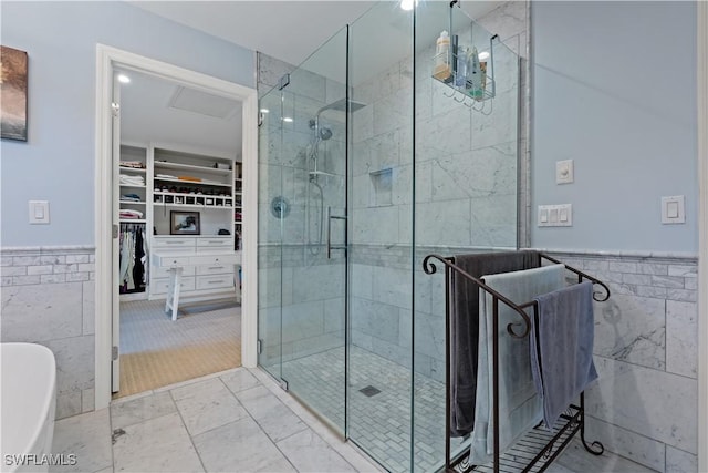 bathroom with a spacious closet, a shower stall, tile walls, and a freestanding tub