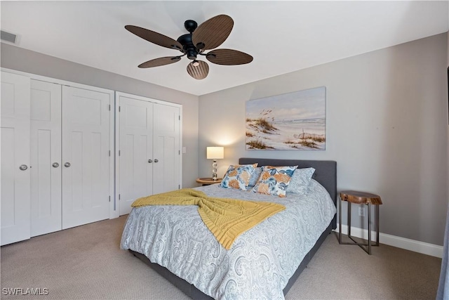 carpeted bedroom featuring visible vents, baseboards, multiple closets, and a ceiling fan