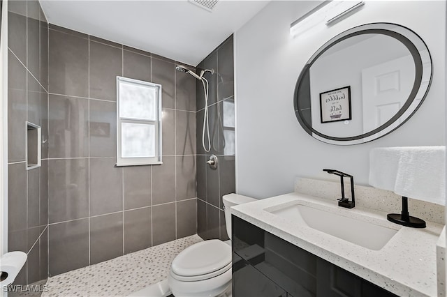 bathroom with visible vents, toilet, vanity, and a tile shower