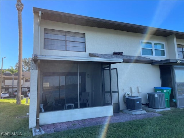 back of property with stucco siding, a lawn, central AC, and a sunroom