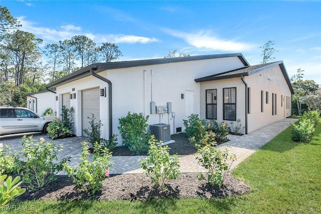 view of front of home featuring a front yard, driveway, stucco siding, a garage, and central air condition unit