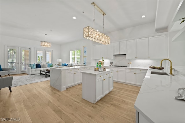 kitchen with a sink, open floor plan, french doors, light wood-type flooring, and a center island