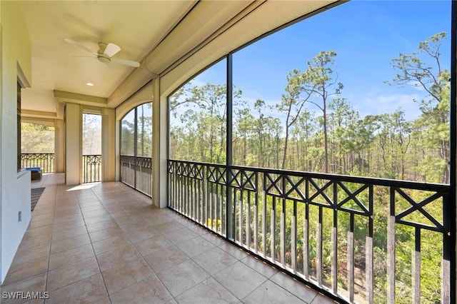 unfurnished sunroom featuring a wooded view and ceiling fan