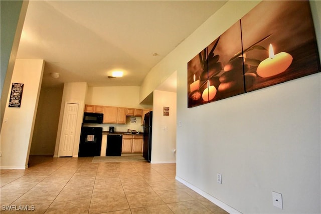 kitchen featuring light tile patterned floors, light brown cabinets, baseboards, black appliances, and dark countertops