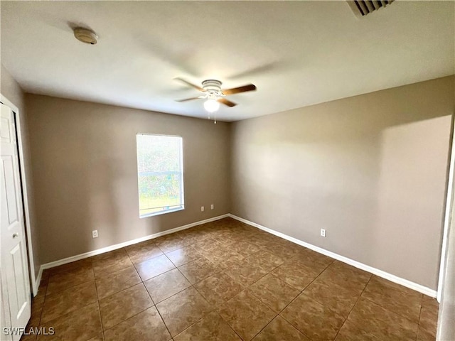 spare room featuring tile patterned flooring, visible vents, a ceiling fan, and baseboards