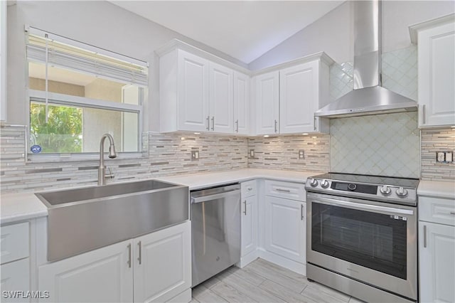 kitchen featuring wall chimney range hood, light countertops, lofted ceiling, appliances with stainless steel finishes, and a sink