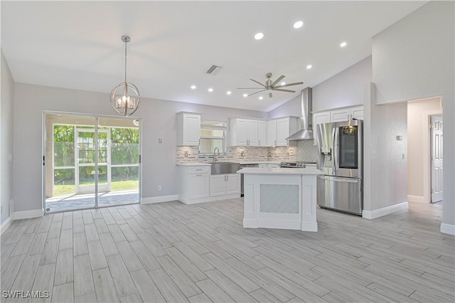 kitchen featuring visible vents, stainless steel refrigerator with ice dispenser, a sink, backsplash, and wall chimney exhaust hood